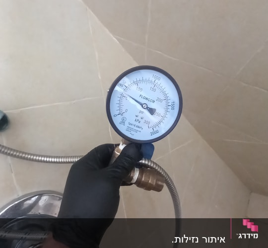 מד לחץ מחובר לצינור מתכת ביד עם כפפה שחורה